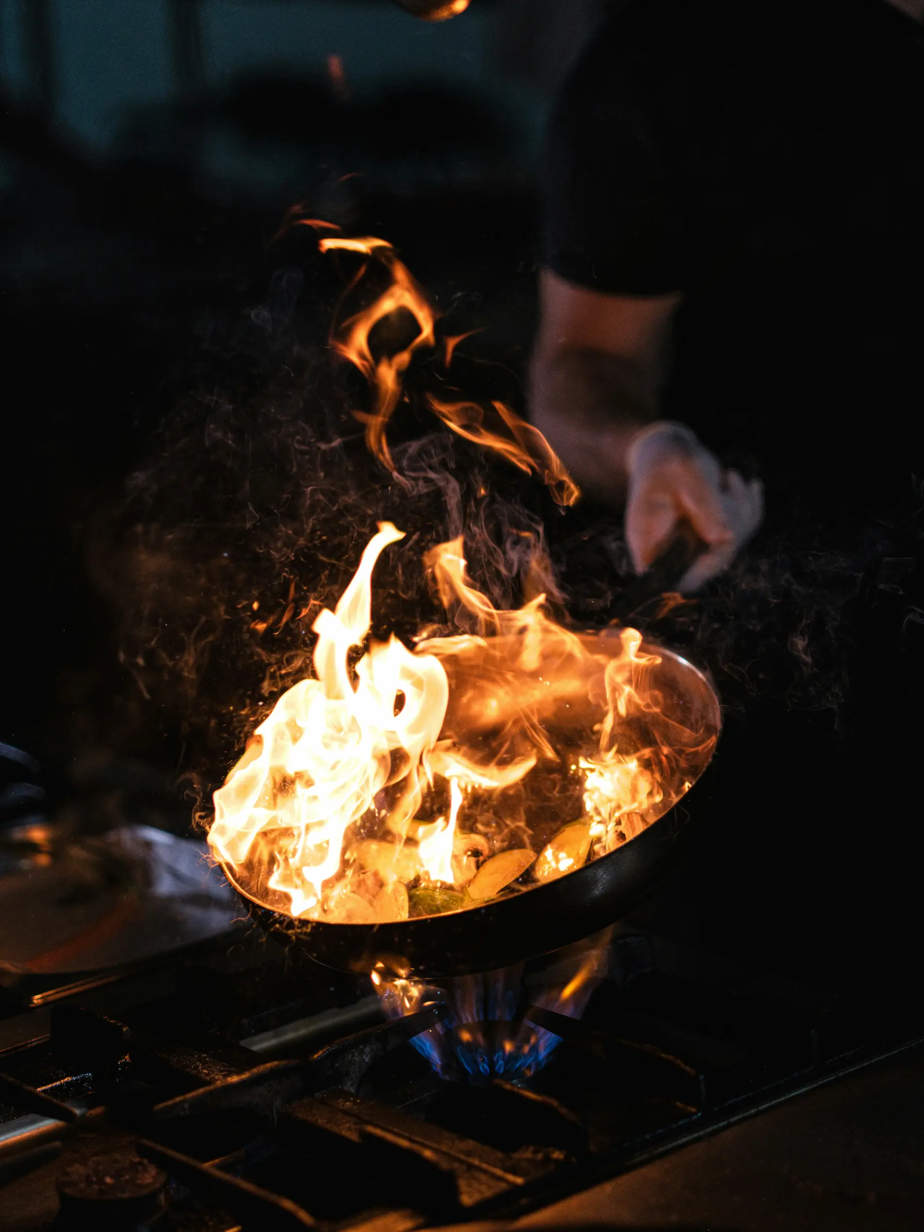 Cocinero salteando en una sartén con llamas en la cocina de La Mesa de Olmo